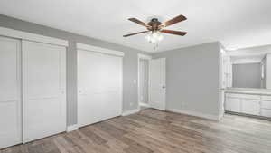 Unfurnished bedroom featuring light hardwood / wood-style flooring, two closets, connected bathroom, and ceiling fan