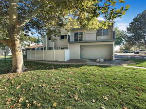 Rear view of property with a balcony, a garage, and a lawn