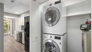 Laundry area featuring a notable chandelier, stacked washer and dryer, and light wood-type flooring