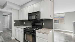 Kitchen with black appliances, decorative backsplash, and white cabinets