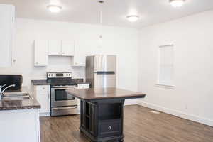 Kitchen featuring hanging light fixtures, dark hardwood / wood-style flooring, white cabinetry, sink, and stainless steel appliances