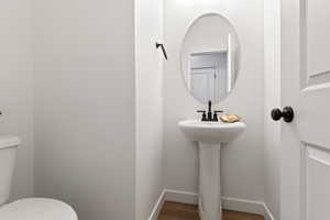 Half bathroom featuring wood finished floors, toilet, and baseboards