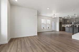 Unfurnished living room featuring baseboards, stairway, an inviting chandelier, and wood finished floors