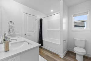 Full bathroom featuring dual vanity, shower / bath combo with shower curtain, hardwood / wood-style flooring, and toilet