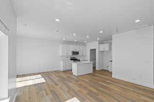 Living Room, Dining area, & Kitchen featuring appliances with stainless steel finishes, white cabinetry, light hardwood / wood-style floors, and an island with sink