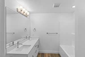 Bathroom featuring dual vanity, tub/ shower, and wood-type flooring