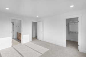 *Photo is of a previously built home of the same layout* Primary bedroom with a closet, a walk in closet, ensuite bath, and light colored carpet