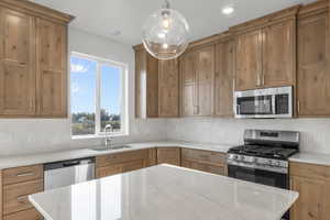 *Photo is of a previously built home of the same layout* Kitchen featuring light stone countertops, appliances with stainless steel finishes, sink, pendant lighting, and decorative backsplash