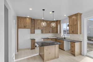 Kitchen with a center island, sink, hanging light fixtures, light wood-type flooring, and tasteful backsplash