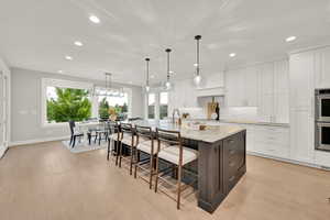 Kitchen with white cabinetry, a kitchen island with sink, light stone countertops, light hardwood / wood-style floors, and decorative light fixtures