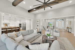 Living room featuring a towering ceiling, beamed ceiling, light hardwood / wood-style flooring, and ceiling fan