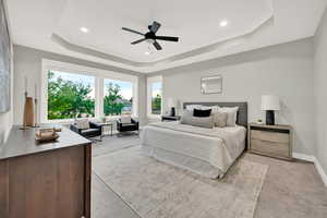 Carpeted bedroom featuring ceiling fan and a raised ceiling