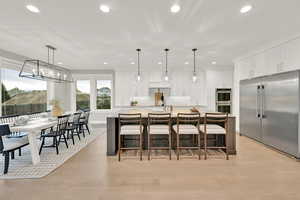 Kitchen featuring a large island with sink, appliances with stainless steel finishes, hanging light fixtures, and white cabinets