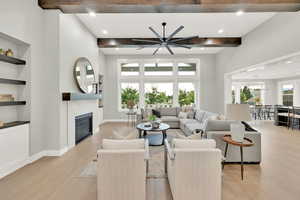 Living room with light hardwood / wood-style flooring, beamed ceiling, built in shelves, and ceiling fan