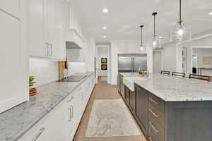 Kitchen featuring high end refrigerator, sink, light wood-type flooring, a large island, and white cabinets