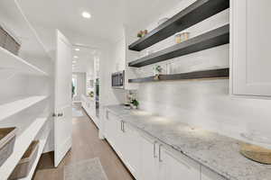 Bar with light stone counters, stainless steel appliances, light hardwood / wood-style flooring, and white cabinets