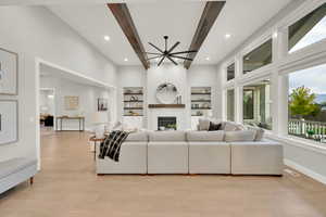 Living room with beam ceiling, ceiling fan, a high ceiling, built in shelves, and light hardwood / wood-style floors