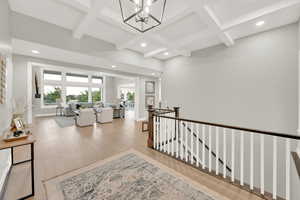 Hall featuring a notable chandelier, light hardwood / wood-style floors, coffered ceiling, and beam ceiling