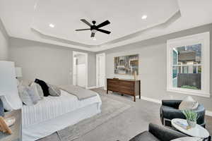 Bedroom with light carpet, a raised ceiling, and ceiling fan