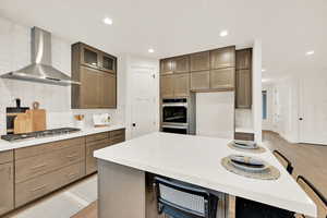 Kitchen with wall chimney exhaust hood, a center island, stainless steel appliances, and light wood-type flooring