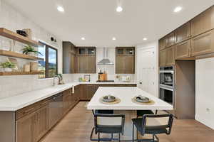 Kitchen with a kitchen island, appliances with stainless steel finishes, wall chimney range hood, and light wood-type flooring