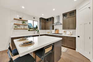 Kitchen featuring a kitchen island, a kitchen breakfast bar, stainless steel gas stovetop, light wood-type flooring, and wall chimney exhaust hood