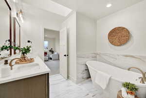 Primary Bathroom featuring vanity, a tub to relax in, and tile walls