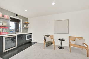 Loft game room Bar with stainless steel microwave, sink, beverage cooler, and dark colored carpet