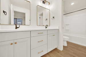 Full bathroom with vanity, toilet, washtub / shower combination, and hardwood / wood-style floors