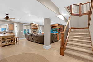 Downstairs living room featuring a stone fireplace, ornamental molding, light wood-type flooring, and ceiling fan