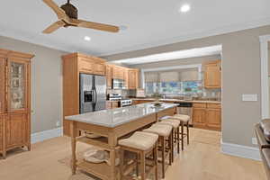 Downstairs, secondary, kitchen featuring a breakfast bar area, appliances with stainless steel finishes, light stone countertops, light brown cabinetry, and light wood-type flooring