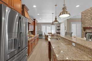 Kitchen featuring light stone countertops, appliances with stainless steel finishes, sink, hanging light fixtures, and light hardwood / wood-style flooring