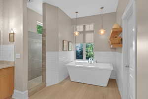 Bathroom featuring vanity, tile walls, wood-type flooring, and plus walk in shower