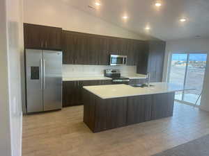 Kitchen featuring lofted ceiling, a center island with sink, light hardwood / wood-style flooring, sink, and stainless steel appliances