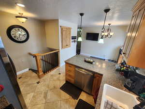 Kitchen with sink, stainless steel dishwasher, light tile patterned floors, stone countertops, and pendant lighting