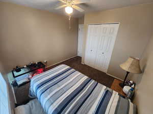 Bedroom with a textured ceiling, a closet, dark carpet, and ceiling fan