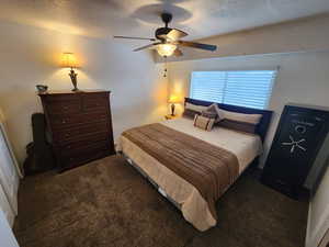 Bedroom featuring ceiling fan, dark colored carpet, and a textured ceiling