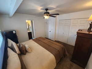 Carpeted bedroom featuring beam ceiling, ceiling fan, and a closet