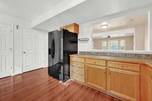 Kitchen with black fridge with ice dispenser, hardwood / wood-style flooring, and ceiling fan