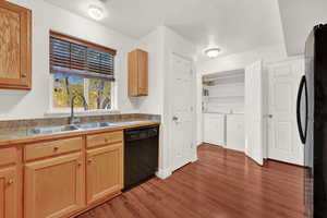 Kitchen with black appliances, washer and dryer, sink, and dark wood-type flooring