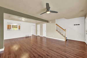 Unfurnished living room featuring a textured ceiling, ceiling fan, and dark wood-type flooring