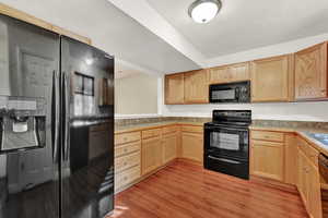 Kitchen with light brown cabinets, sink, light hardwood / wood-style flooring, and black appliances