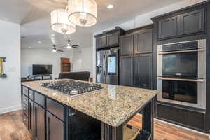 Kitchen with dark brown cabinets, a center island, stainless steel appliances, light stone counters, and light hardwood / wood-style flooring