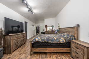 Bedroom featuring lofted ceiling, a textured ceiling, hardwood / wood-style flooring, and track lighting