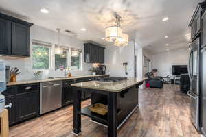 Kitchen with wood-type flooring, sink, decorative light fixtures, appliances with stainless steel finishes, and light stone counters