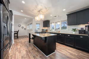 Kitchen with a kitchen island, a breakfast bar area, stainless steel appliances, decorative light fixtures, and light wood-type flooring