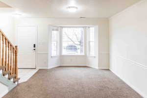 Carpeted entrance foyer with a textured ceiling and ornamental molding