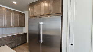 Kitchen with high end fridge, light hardwood / wood-style floors, and a textured ceiling