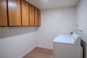 Washroom featuring light hardwood / wood-style flooring, washer and dryer, and cabinets