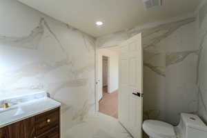 Bathroom featuring toilet, vanity, and tile walls